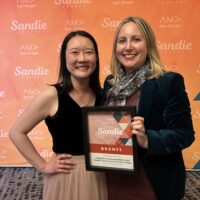 Sandy Young and Molly Pincherli hold the AMA Sandie award in front of an orange background